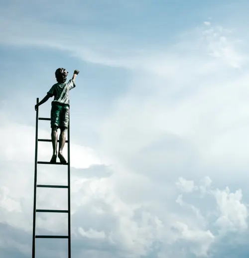 Barn som står på toppen av en stige og ser og strekker seg mot himmelen
